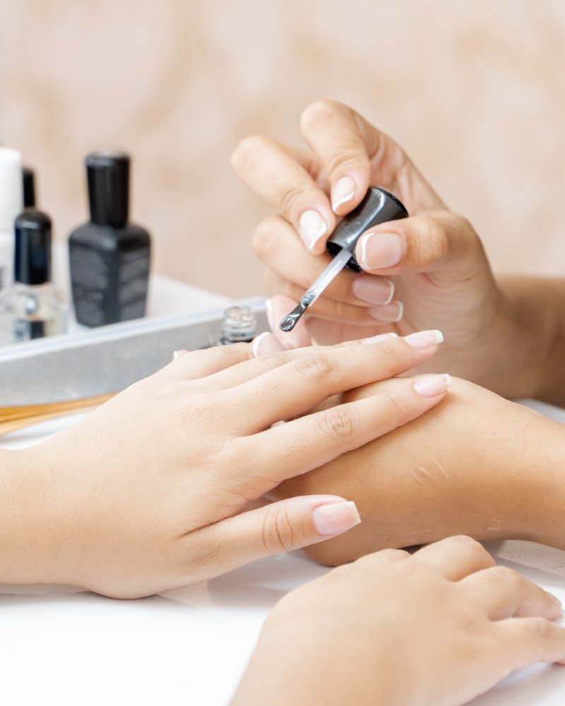A technician painting a client's nails, polish bottles lined up on the table