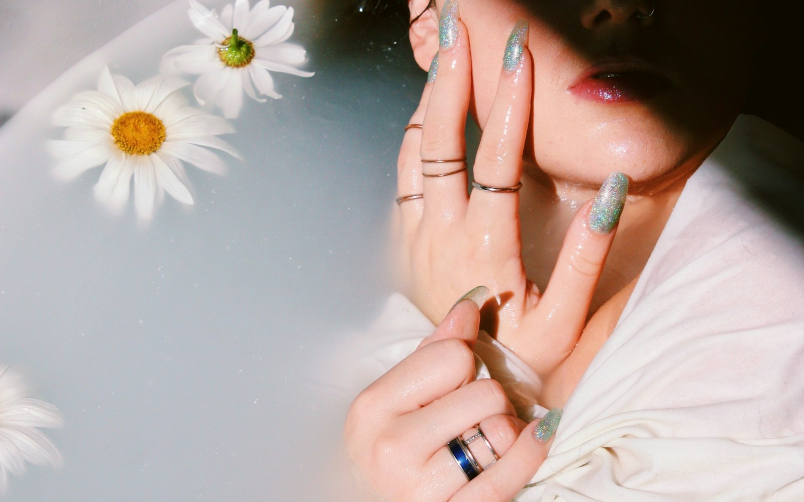 Hands resting in milky water scattered with daisies