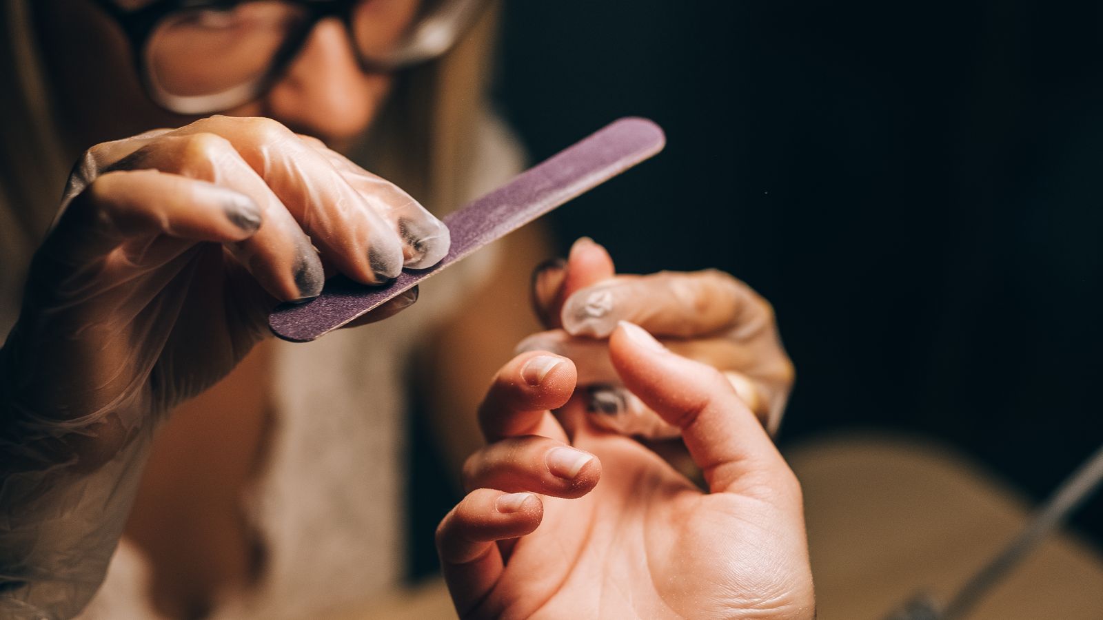 A technician filing a client's nails at the studio table