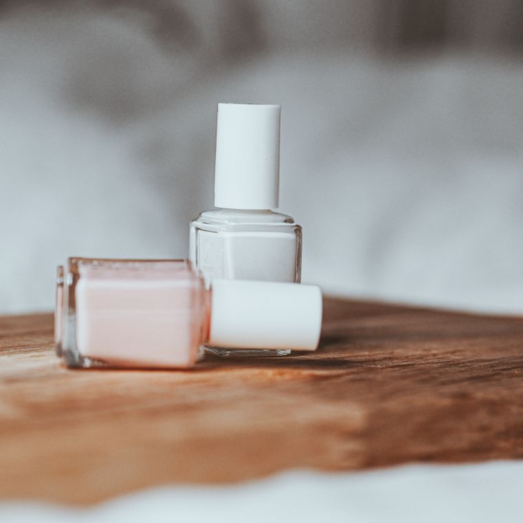 Two bottles of pale pink and white polish on a wooden table