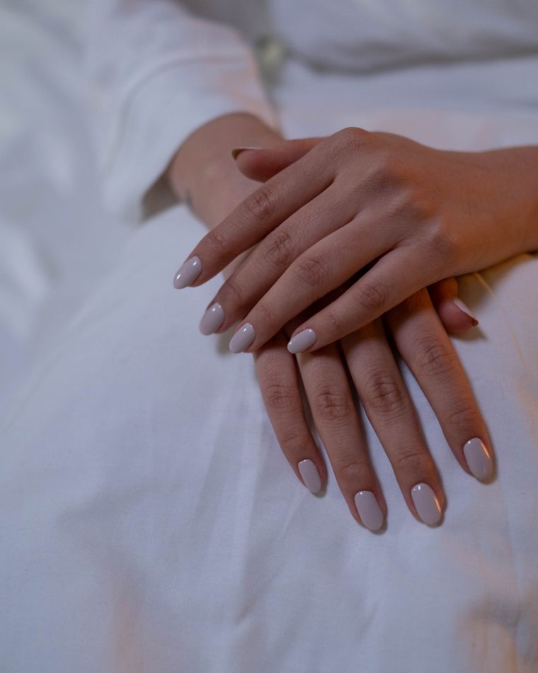 Hands with soft neutral nails resting on white linen