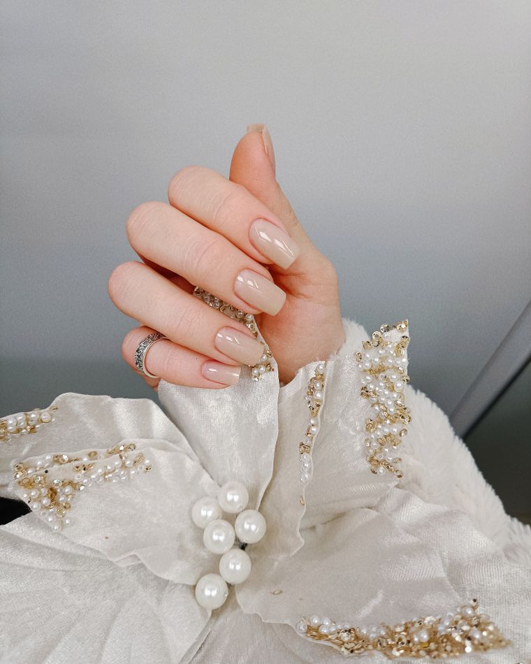 A hand with pearl-detailed nails resting on ivory lace