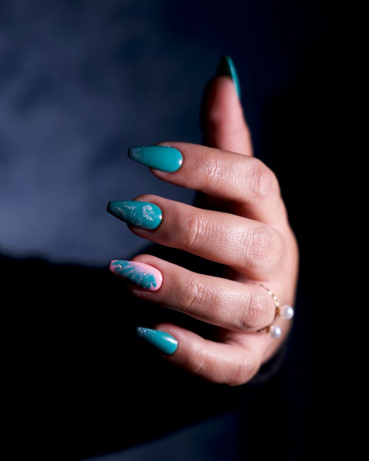 A hand with teal cateye nails photographed against deep blue
