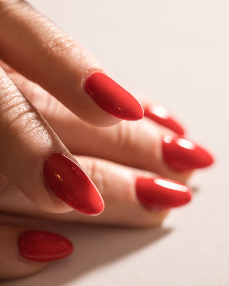 A hand with glossy red almond nails on a cream background