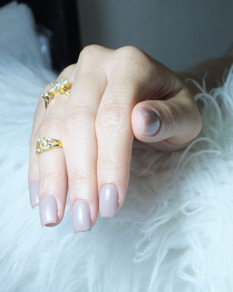 A hand with sheer nude nails and stacked gold rings on a soft throw
