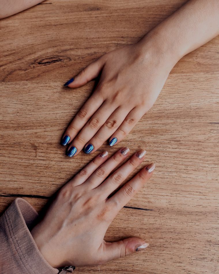 Two hands with slate and clay coloured nails resting on a wooden table