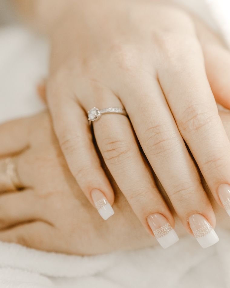 A bride's hands with a classic pale manicure and an engagement ring