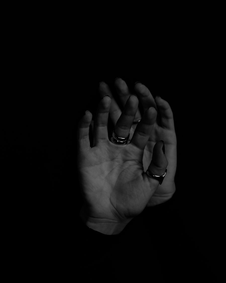 Two hands resting together, photographed in black and white, wearing plain bands.