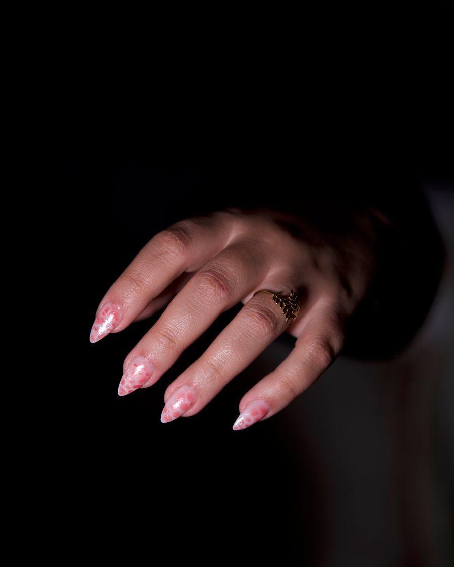 A hand with a fine ivory French manicure and a gold signet ring against black.