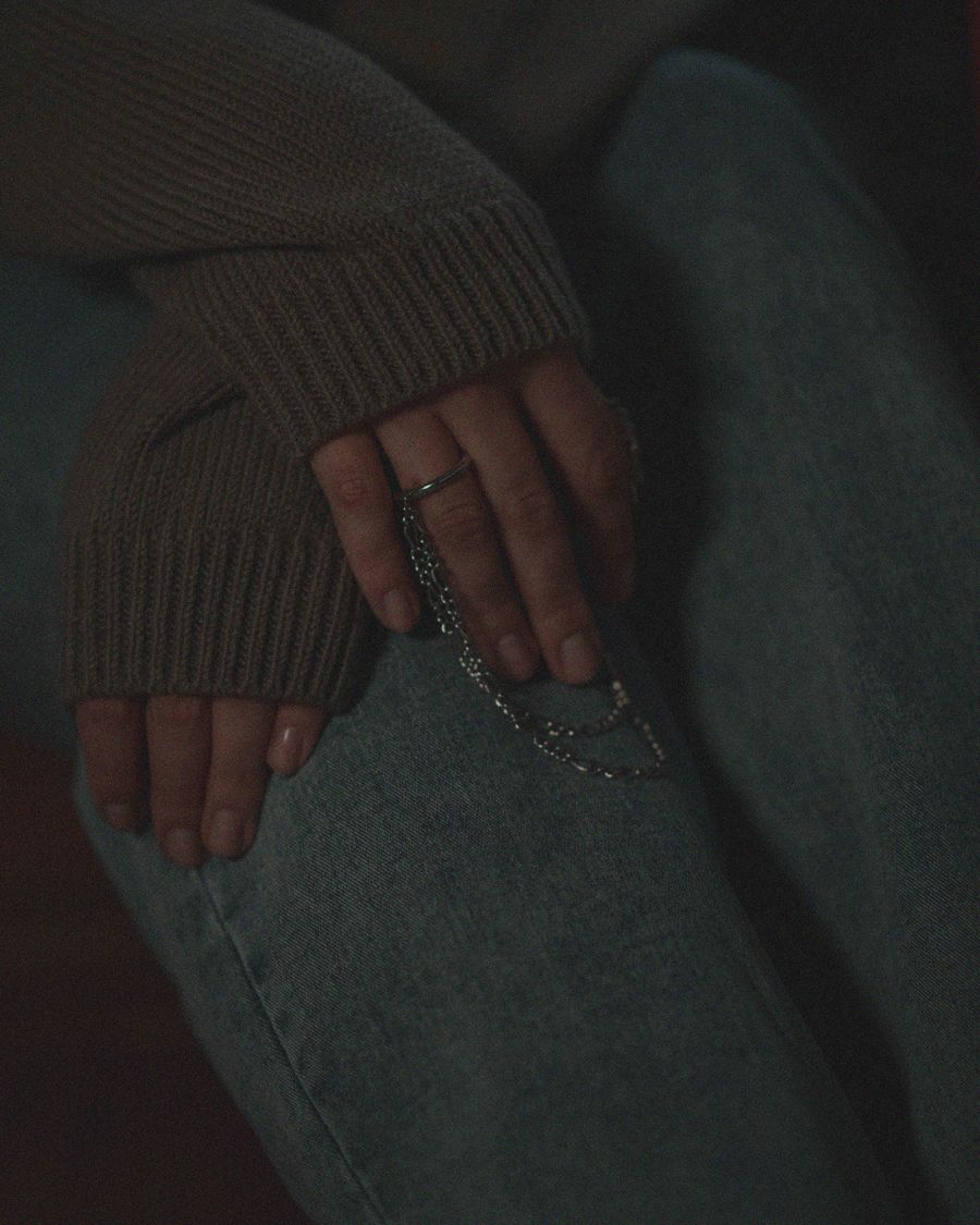 A hand resting inside a dark knitted sleeve, nails shaped short.
