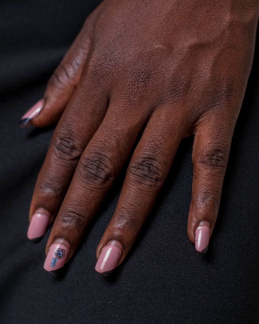 A hand with pale nude nails resting on black fabric.