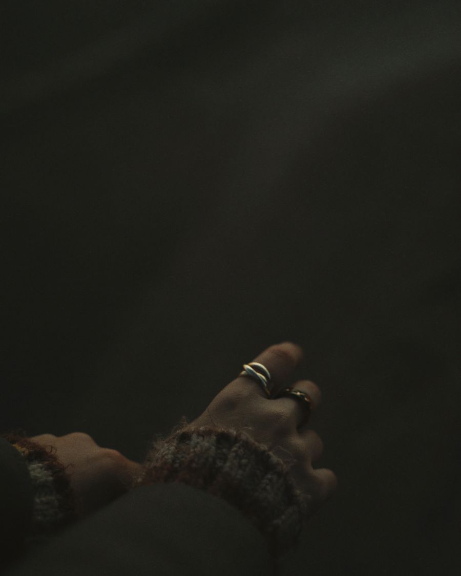 Hands wearing stacked rings, lit low against a dark ground.