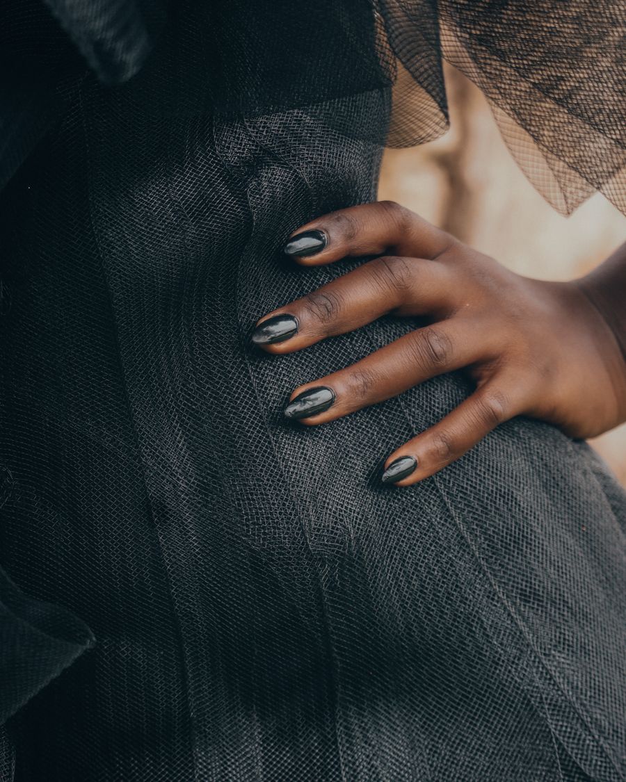 A hand with dark chrome nails against pleated black fabric.