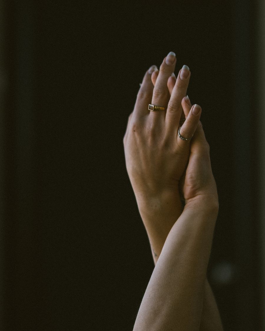Two hands raised together against a dark olive ground, wearing a single ring.