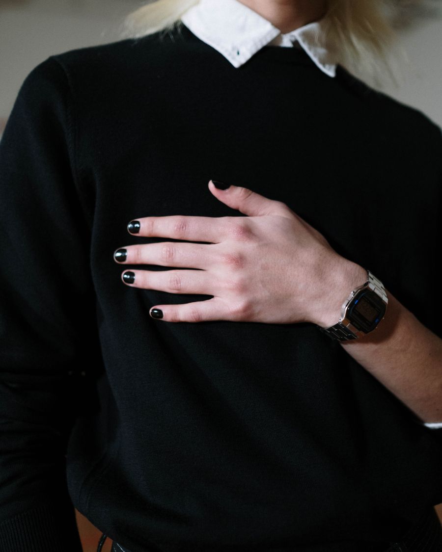 A hand with very dark polish resting against a black knitted sweater.
