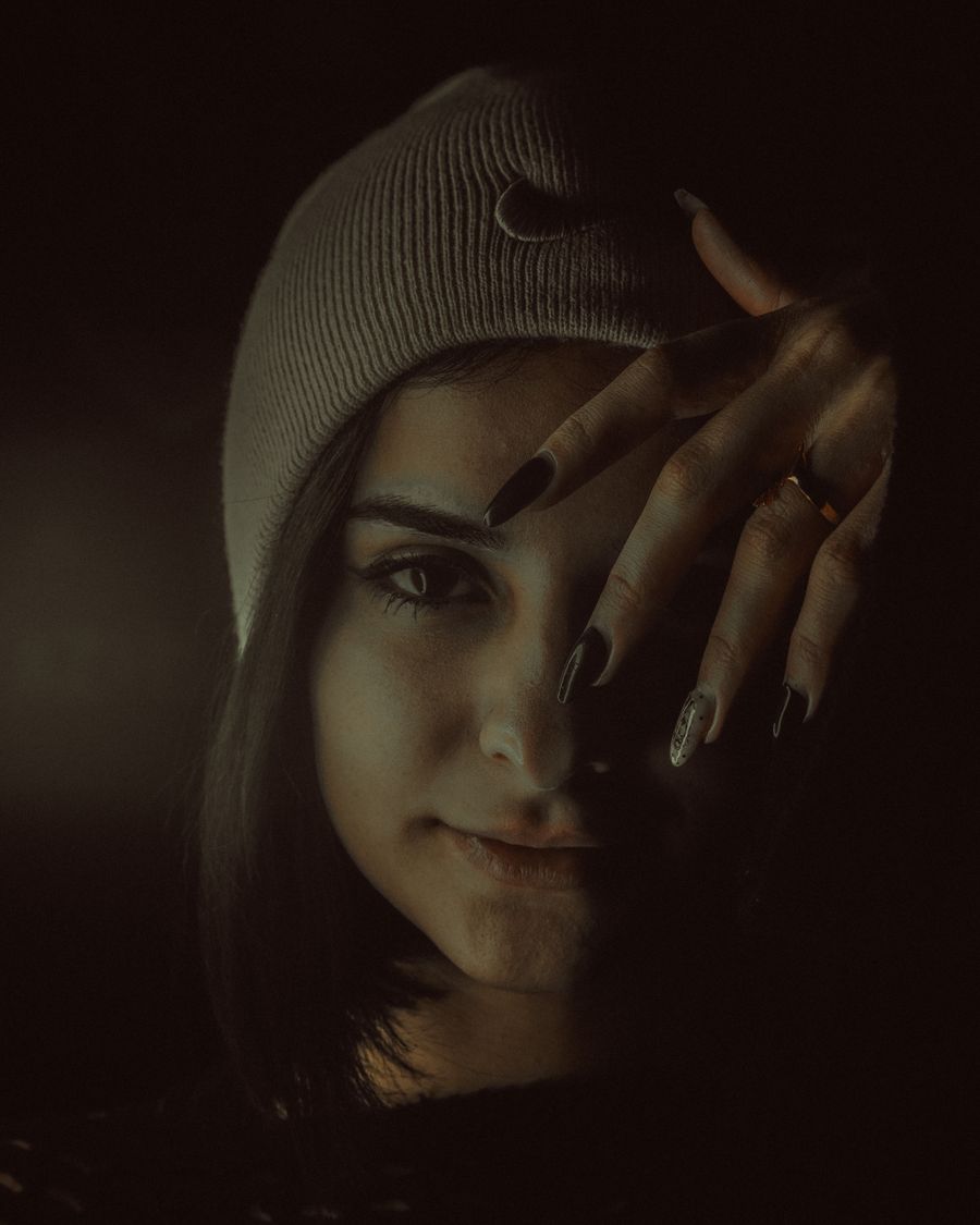 A low-lit portrait, a hand with decorated nails raised beside the face.
