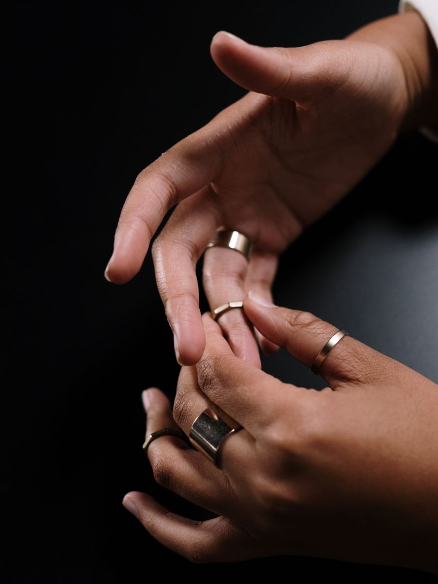 Two hands wearing fine rings, photographed close and low-lit against black.