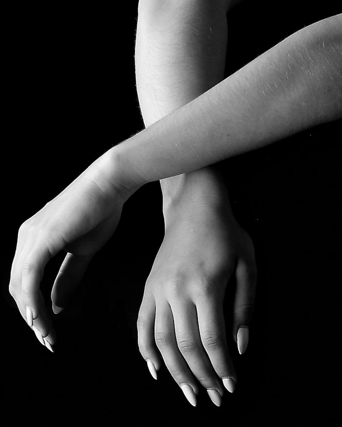 A pair of hands and forearms crossed against a black background