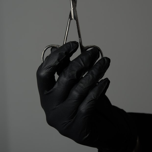 A gloved hand holding a pair of fine cuticle scissors