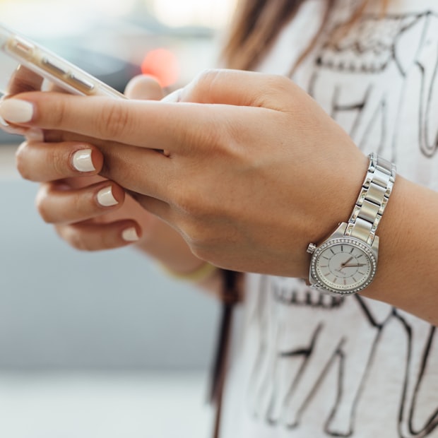 A hand with a pale manicure and a wristwatch resting on a magazine