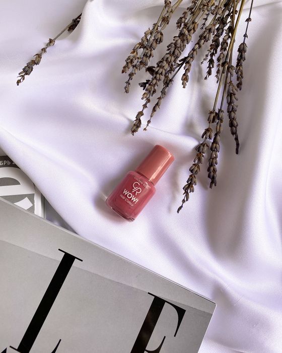A bottle of dusty pink polish beside dried lavender on a magazine