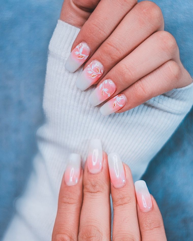 Hands with long nails painted in a soft pink french with white floral line work, resting on a pale blue jumper