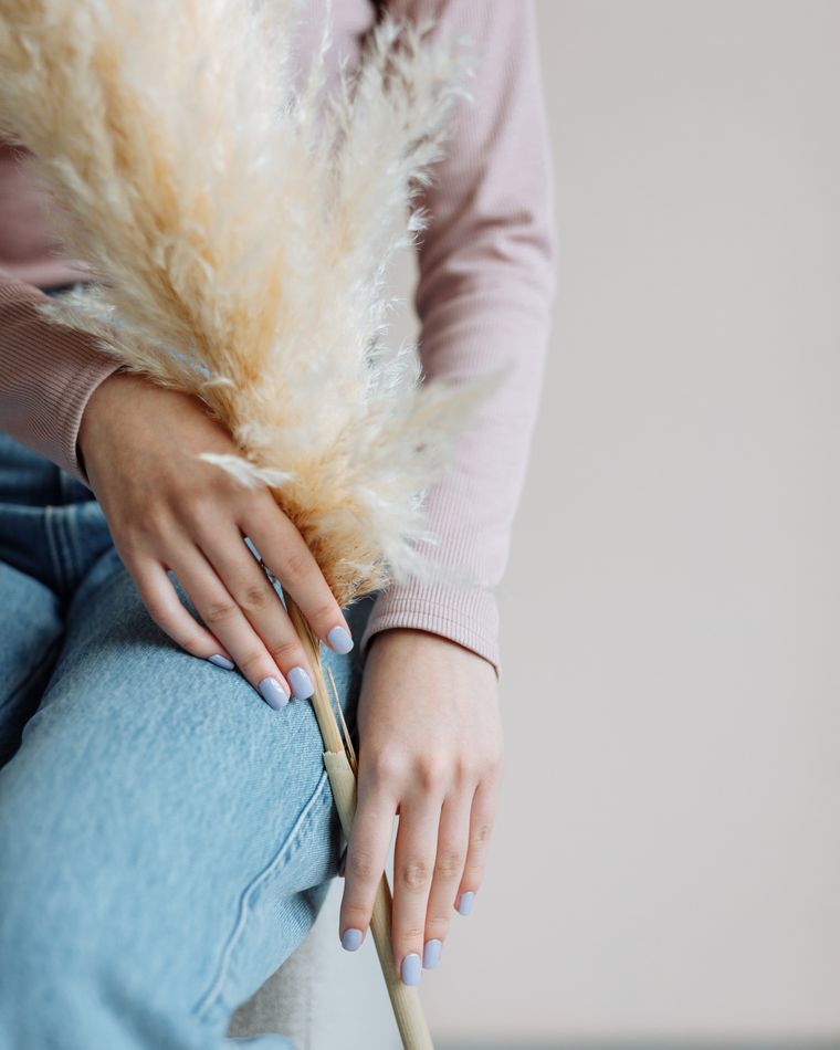 A person in a pale pink jumper holding dried pampas grass, hands with neutral nails