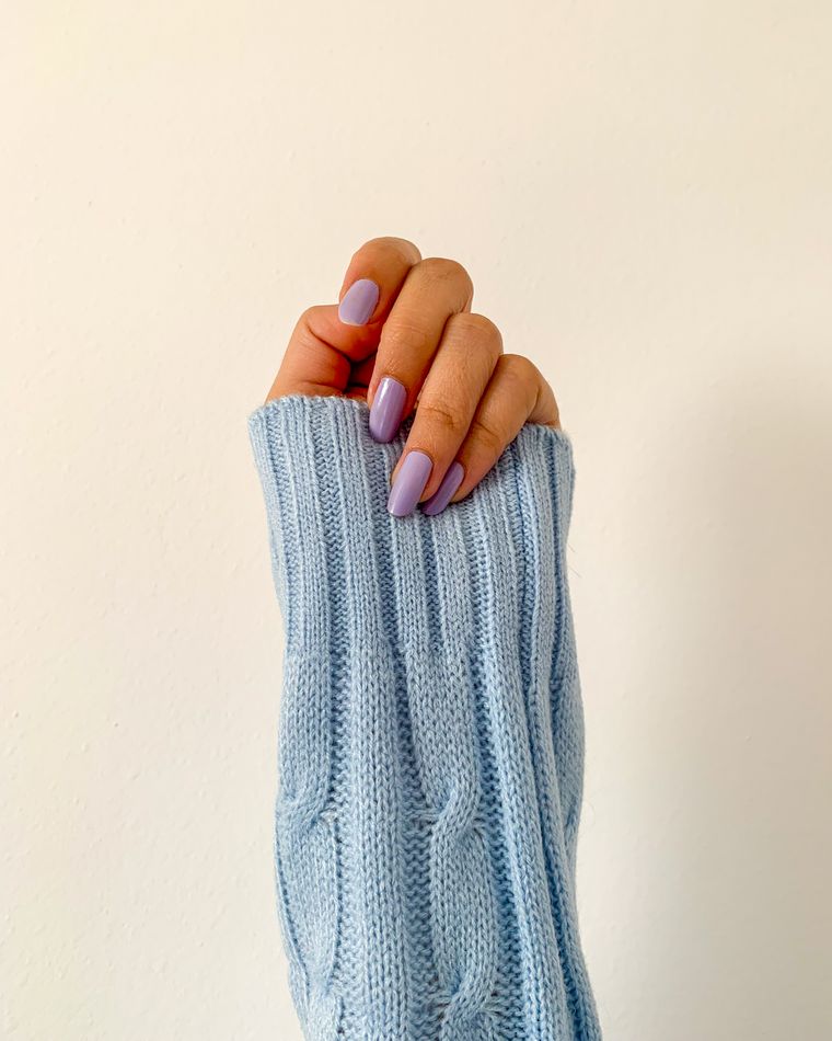 A hand with soft peach and lilac nails resting over a pale blue knitted sleeve