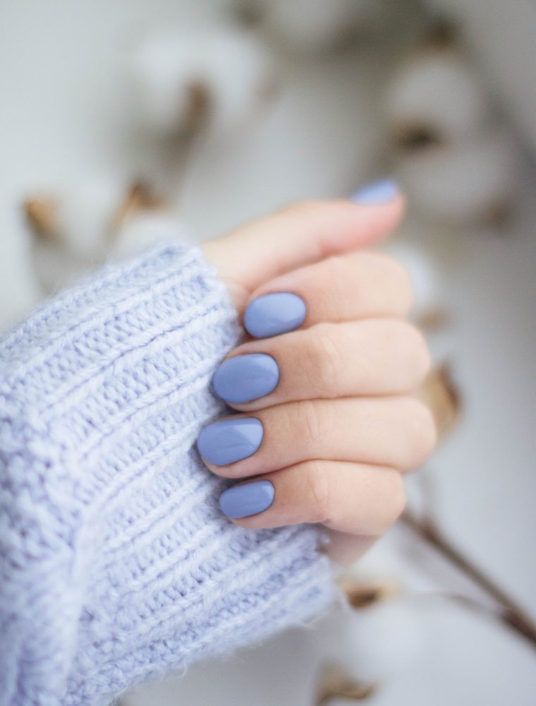 A hand with lilac nails resting against a white knitted sleeve