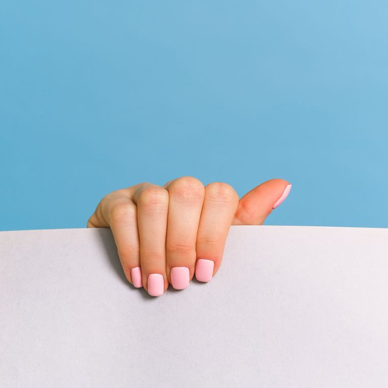 A hand with coral and cream nails against a bright blue background