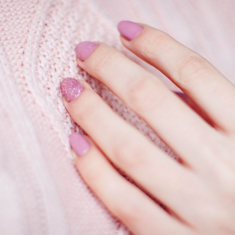 A hand with pink nails resting on a soft pink knitted sleeve