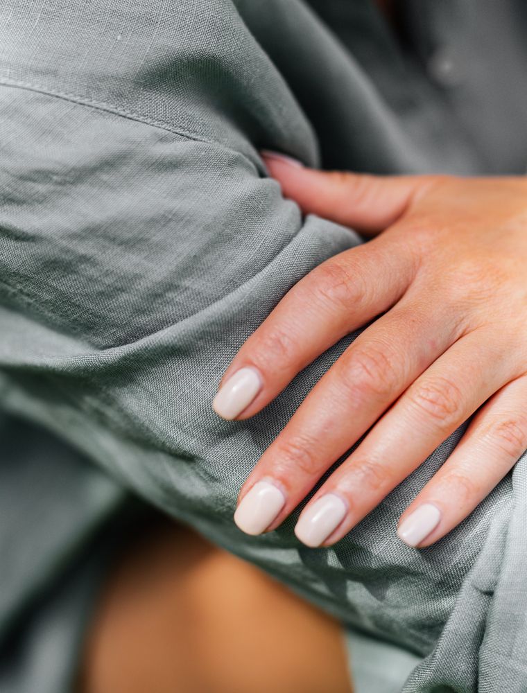 Hands with bare buffed nails resting on a sage green linen dress