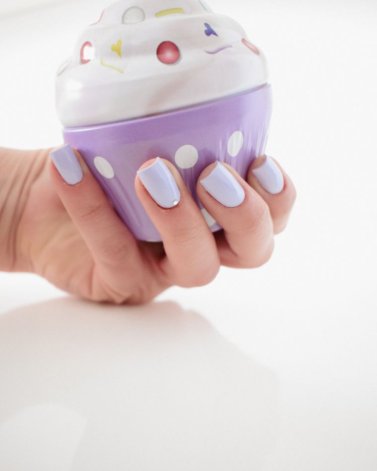 A hand with powder blue nails holding a lilac cupcake-shaped toy