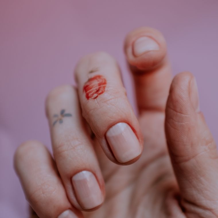 A hand with sheer nails and small line-work accents on a pink backdrop