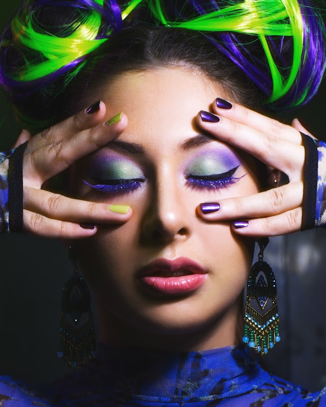 A portrait under green and violet light, hands raised beside the face