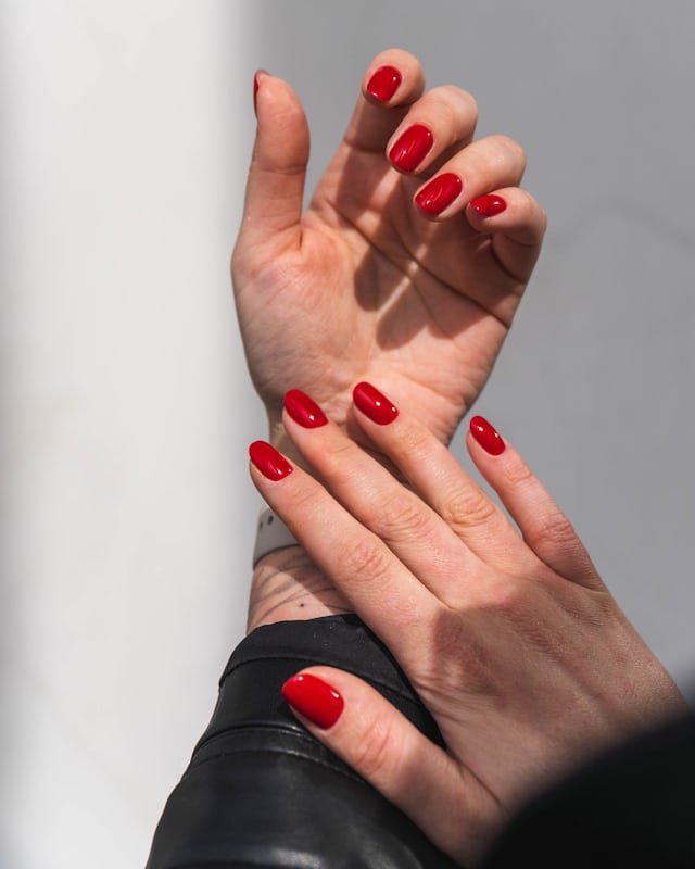 A hand with glossy red nails against a black leather jacket
