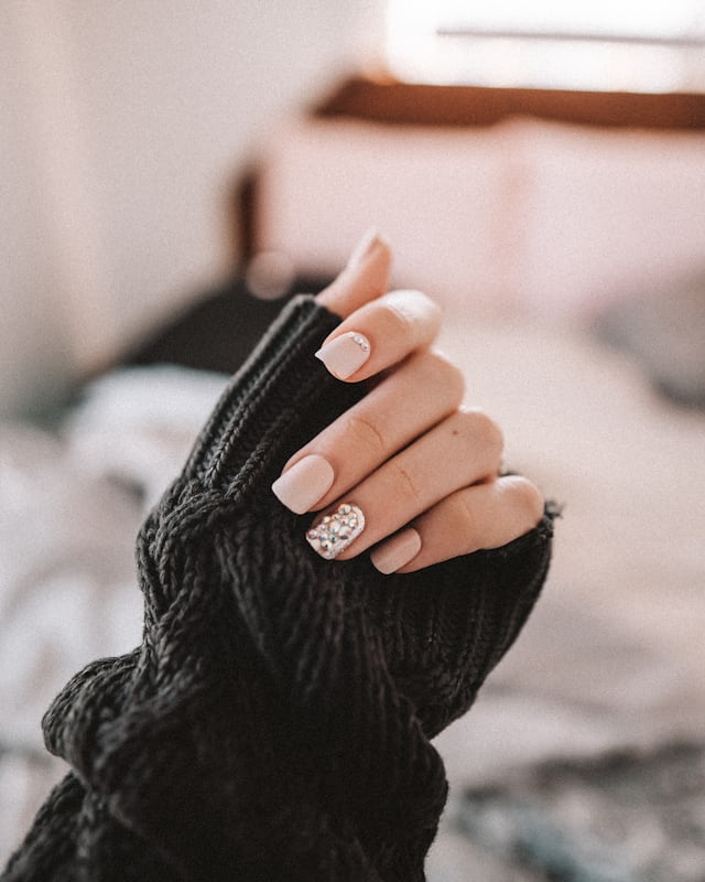 A hand with pale iridescent nails resting on a black leather sleeve
