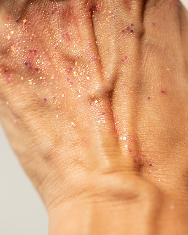 A hand dusted with fine gold and pink glitter, close up